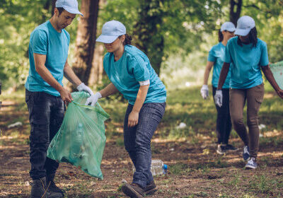 Group of four people wearing blue shirts gathering trash and cleaning up an outdoor area.